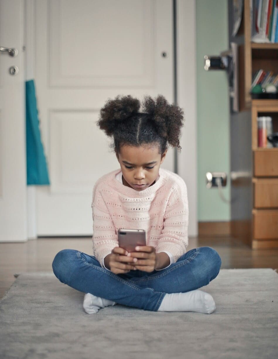 Petit fille assise en tailleur absorbée par un smartphone